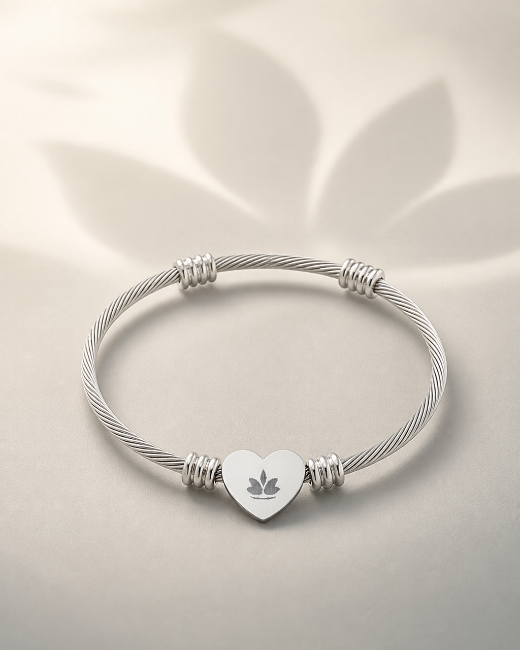 Silver-tone heart cuff bracelet with centered lotus engraving on a warm ivory background