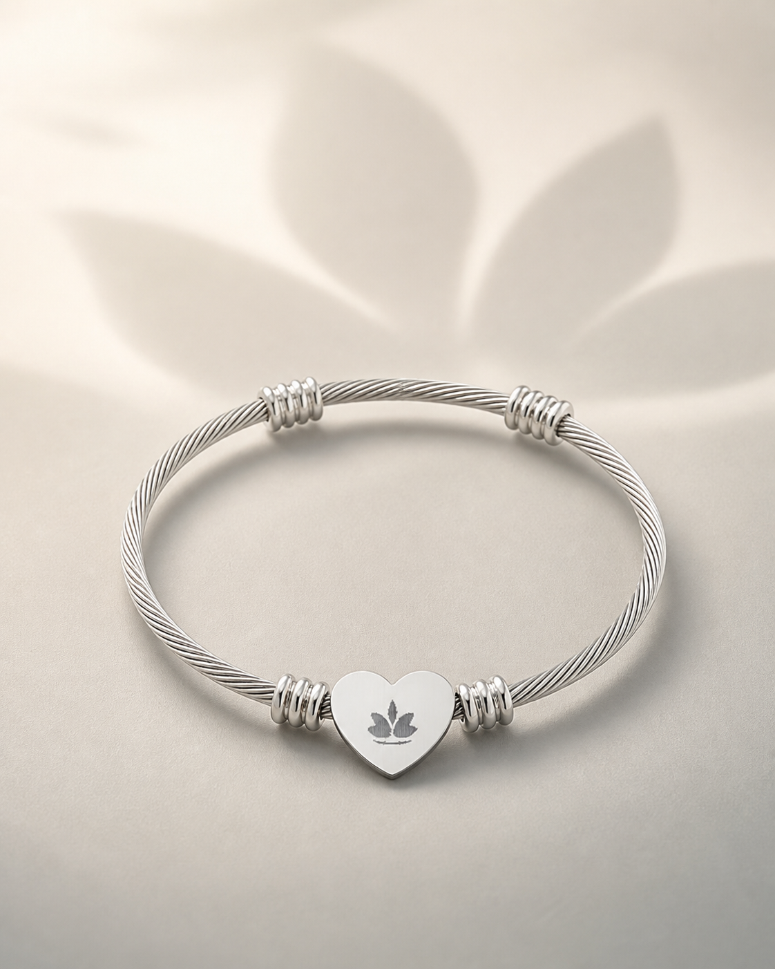 Silver-tone heart cuff bracelet with centered lotus engraving on a warm ivory background
