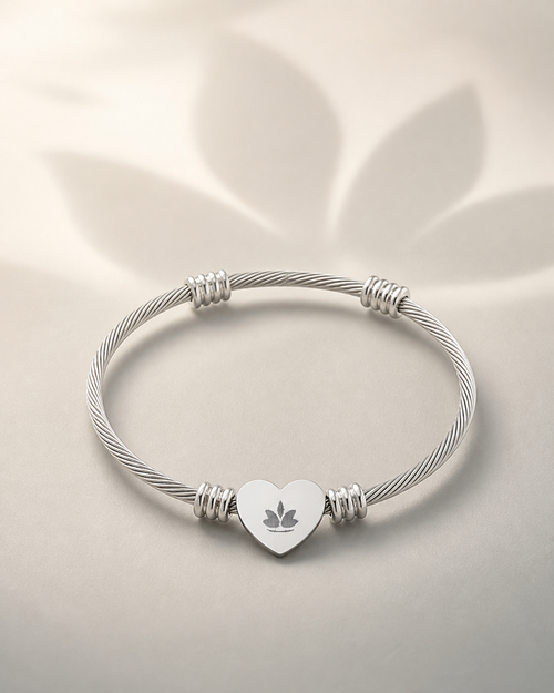 Silver-tone heart cuff bracelet with centered lotus engraving on a warm ivory background