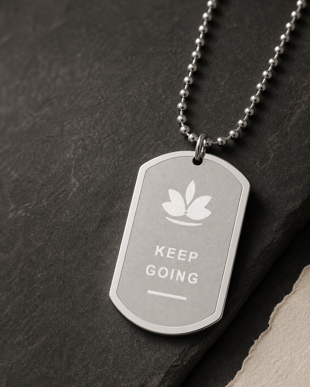 Styled view of silver-tone stainless steel dog tag necklace with fixed lotus and KEEP GOING design